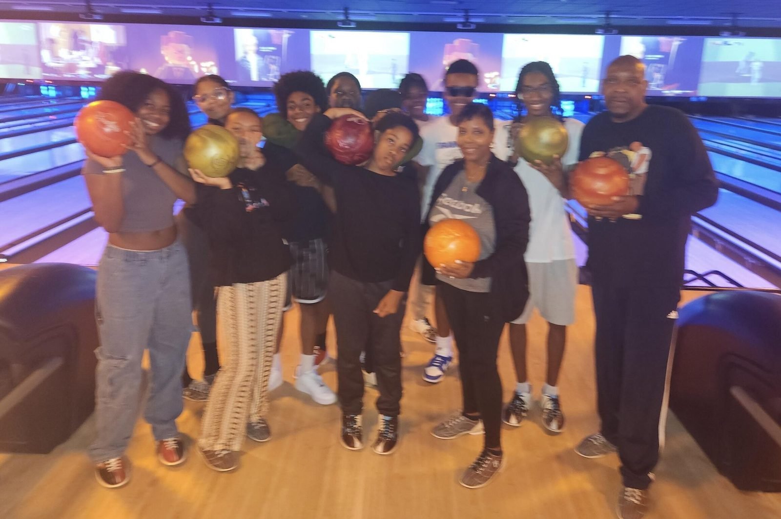 A group of CCWW teens and mentors holding bowling balls at a bowling alley outing